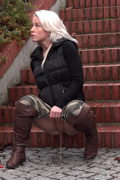 A blonde in camouflage leggings pulls them down and pisses in a straight line onto the ground.